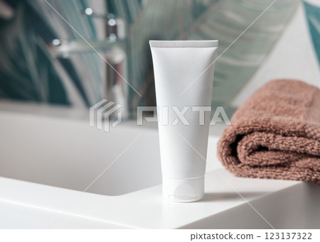 White cream tube near brown folded towels on basin in tropical bathroom close up, cosmetic mockup White cream tube near brown folded towels on basin in tropical bathroom close up, cosmetic mockup 123137322