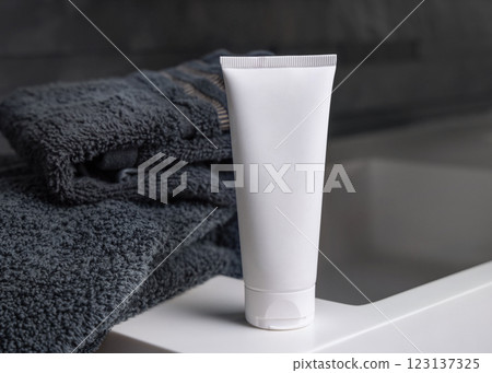 White cream tube near black folded towels on basin in dark grey bathroom close up, cosmetic mockup 123137325