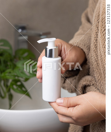 Close up of hands in brown bathrobe pumping soap from a cosmetic bottle, mockup Close up of hands in brown bathrobe pumping soap from a cosmetic bottle, mockup 123137338