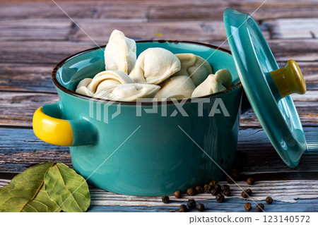 Raw dumplings in a blue bowl on a wooden background. Raw dumplings in a blue bowl on a wooden background. 123140572