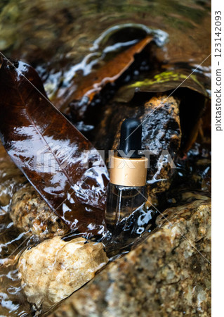 A hydration serum bottle sits on stone, surrounded by leaves and flowing water. A hydration serum bottle sits on stone, surrounded by leaves and flowing water. 123142093
