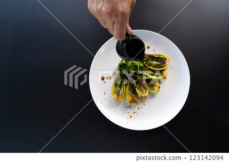 A hand pours sauce over fresh bok choy arranged on a plate, highlighting Asian cooking techniques. 123142094