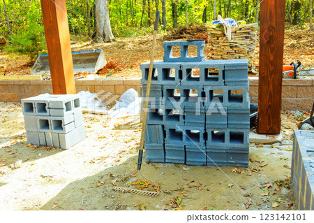Concrete blocks are stacked at construction site amid trees, highlighting building materials, tools. 123142101