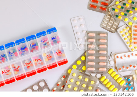 Pills organizer filled for each day of week sits alongside various colorful medication tablets, ready for use. Pills organizer filled for each day of week sits alongside various colorful medication tablets, ready for use. 123142106