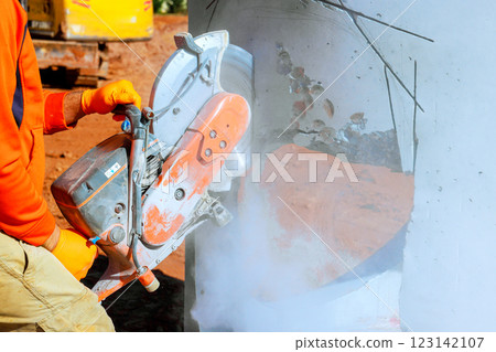 Worker uses concrete cutter, shaping drainage system creating dust on construction site Worker uses concrete cutter, shaping drainage system creating dust on construction site 123142107