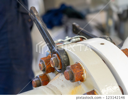Close-up of an industrial flange with bolts being tightened using a wrench for precision and secure operation Close-up of an industrial flange with bolts being tightened using a wrench for precision and secure operation 123142146