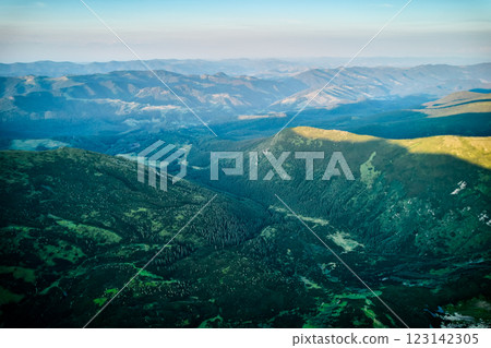Aerial view of rugged mountain range with lush green slopes at sunset. Landscape showcases beauty of untouched nature with distant peaks and valleys bathed in soft sunlight. Carpathians, Chornogora. 123142305