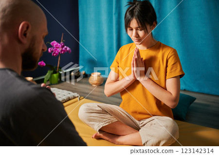 Man and woman sitting on mat facing each other, showing the namaste sign. Masseuse and her client after Thai massage. Focus on a woman. Man and woman sitting on mat facing each other, showing the namaste sign. Masseuse and her client after Thai massage. Focus on a woman. 123142314