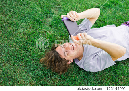 Young man smiling confident playing video game at park lying on a grass. Technology and gaming concept 123143091