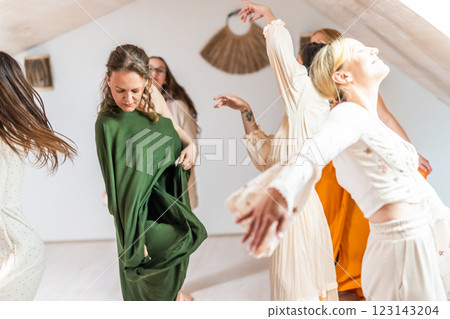 Group of cheerful women all ages, happy people dancing together wearing traditional colorful dresses and hippy clothes. Free people enjoying leisure activity, emphasizing friendship, fun, movement. 123143204