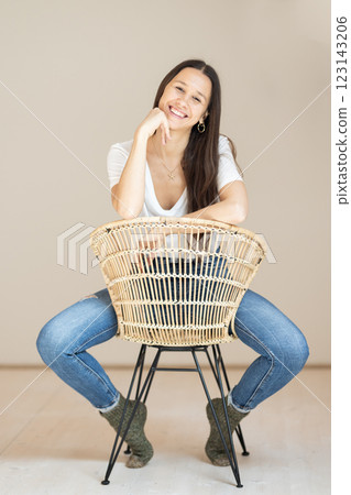 Portrait of confident beautiful woman with long brown hair, wearing casual clothes, sitting on chair in tight jeans and white t-shirt, studio background Portrait of confident beautiful woman with long brown hair, wearing casual clothes, sitting on chair in tight jeans and white t-shirt, studio background 123143206