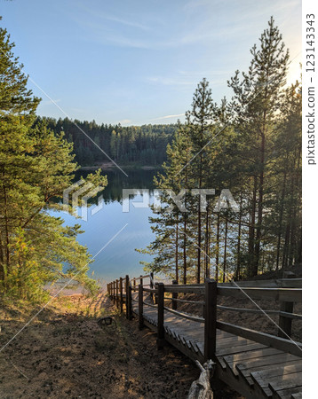 A wooden staircase leads to a tranquil lake surrounded by a lush pine forest in Blue Hills Nature Park, Ogre, Latvia. A wooden staircase leads to a tranquil lake surrounded by a lush pine forest in Blue Hills Nature Park, Ogre, Latvia. 123143343