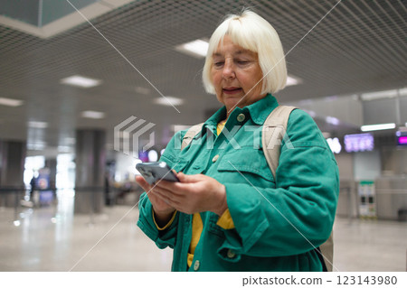 Caucasian 60s smiling business woman in green jacket in international airport, checking her phone while waiting for her flight Caucasian 60s smiling business woman in green jacket in international airport, checking her phone while waiting for her flight 123143980