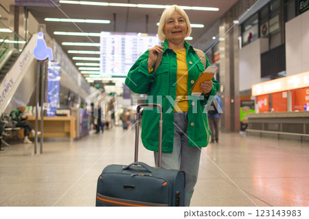 Traveler tourist happy smiling joyful fun mature elderly senior lady woman 55 years old with hand luggage, backpack holds passport and waits for flight travel at international airport terminal. Traveler tourist happy smiling joyful fun mature elderly senior lady woman 55 years old with hand luggage, backpack holds passport and waits for flight travel at international airport terminal. 123143983