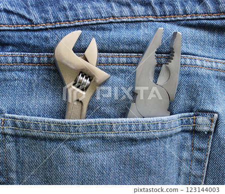 An adjustable spanner and pliers are placed in a jeans pocket. Closeup stock image for home repair theme An adjustable spanner and pliers are placed in a jeans pocket. Closeup stock image for home repair theme 123144003