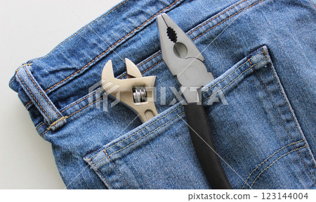 Adjustable wrench and pliers with one untucked handle in a jeans pocket. Detailed stock photo for home tools illustration Adjustable wrench and pliers with one untucked handle in a jeans pocket. Detailed stock photo for home tools illustration 123144004