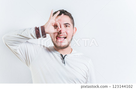 Funny young man making OK gesture looking through fingers isolated. Happy guy making ok gesture looking through fingers Funny young man making OK gesture looking through fingers isolated. Happy guy making ok gesture looking through fingers 123144102