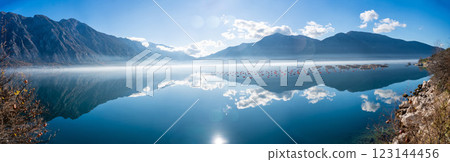 Mountains with clouds and their reflection in the still waters of the sea, separated by a strip of fog in winter morning Bay of Kotor in Montenegro 123144456