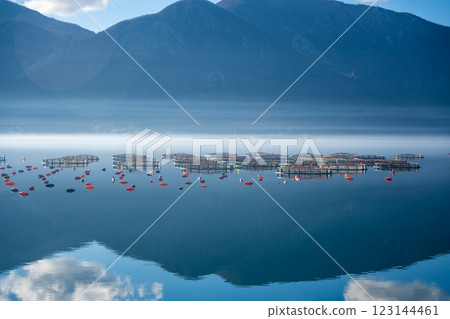 Mountains with clouds and their reflection in the still waters of the sea, separated by a strip of fog in winter morning Bay of Kotor in Montenegro 123144461