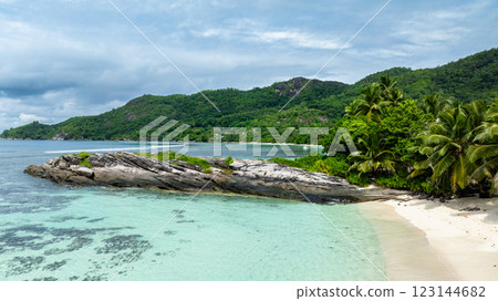 Rocky shoreline surrounded by turquoise waters and a dense tropical forest. Seychelles, Mahe. Anse Forbans. 123144682