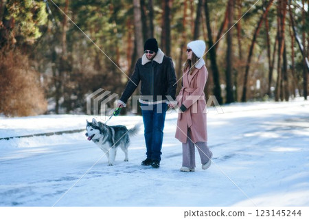 Couple walks a husky dog on a snowy path in winter park 123145244