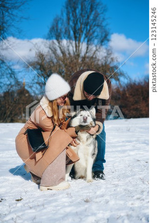 Couple joyfully plays with a dog in snowy park during a sunny day Couple joyfully plays with a dog in snowy park during a sunny day 123145246
