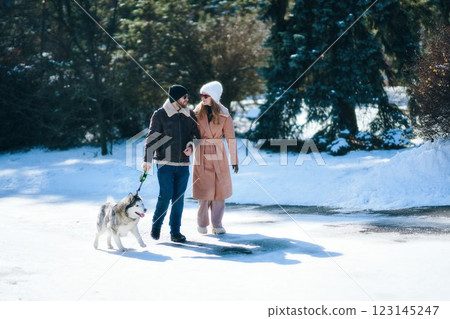 Couple enjoying a winter walk with a husky in a snowy park Couple enjoying a winter walk with a husky in a snowy park 123145247