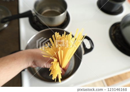 A hand lowers pasta into a saucepan 123146168