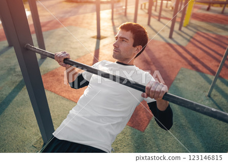 young athletic man exercising at fitness calisthenics workout and do australian pull-ups or inverted rows at street gym during sunset, body improvement and strength training concept 123146815