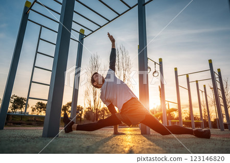young athletic man exercising at fitness calisthenics workout and stretching legs at street gym during sunset, body improvement and strength training concept young athletic man exercising at fitness calisthenics workout and stretching legs at street gym during sunset, body improvement and strength training concept 123146820