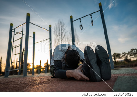 young athletic man exercising at fitness calisthenics workout and stretching legs and back at street gym during sunset, body improvement and strength training concept young athletic man exercising at fitness calisthenics workout and stretching legs and back at street gym during sunset, body improvement and strength training concept 123146823