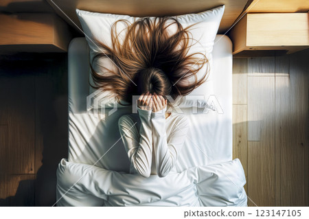 Young woman lying in bed covering face with hands. AI generated 123147105
