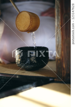 A woman in a kimono is pouring hot water into a black teacup 123147628