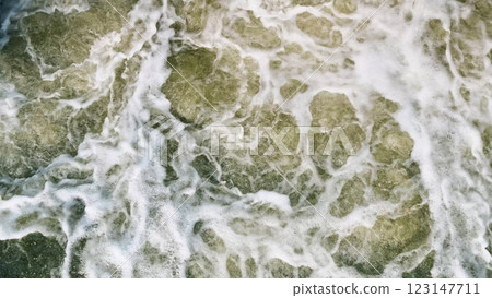 An aerial view captures the swirling ocean waves creating intricate and beautiful foam patterns in the water An aerial view captures the swirling ocean waves creating intricate and beautiful foam patterns in the water 123147711