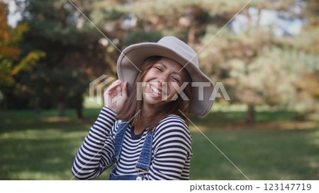 A cheerful woman enjoying the outdoors, wearing a stylish hat and a striped shirt in a lush green setting. A cheerful woman enjoying the outdoors, wearing a stylish hat and a striped shirt in a lush green setting. 123147719
