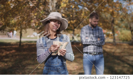 In an autumn park filled with colorful leaves, a smiling woman joyfully holds cash while a man stands behind her 123147725
