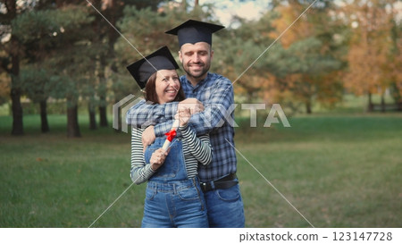 A happy couple celebrating their graduation in a scenic park setting, showcasing their achievements. 123147728