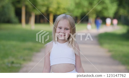 A joyful little girl smiles brightly while walking happily in a serene and peaceful park setting filled with greenery 123147762