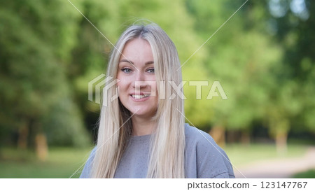 A cheerful young woman with flowing hair is posing joyfully in a vibrant and lush green park, radiating happiness 123147767