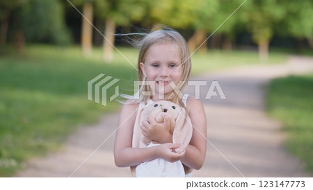 In a serene outdoor setting, a young girl joyfully embraces and cuddles with her plush toy, radiating happiness 123147773
