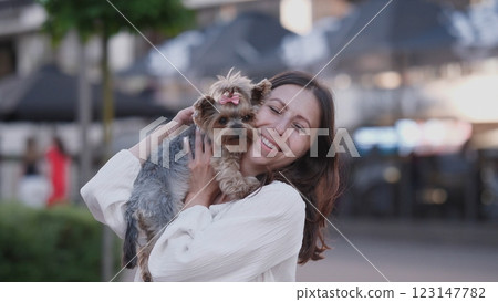 A happy woman holds her beloved dog in a vibrant urban setting, highlighting the joy of companionship A happy woman holds her beloved dog in a vibrant urban setting, highlighting the joy of companionship 123147782