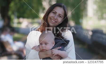 In a serene, vibrant park setting, a joyful mother tenderly embraces her baby, radiating pure love and warmth In a serene, vibrant park setting, a joyful mother tenderly embraces her baby, radiating pure love and warmth 123147795