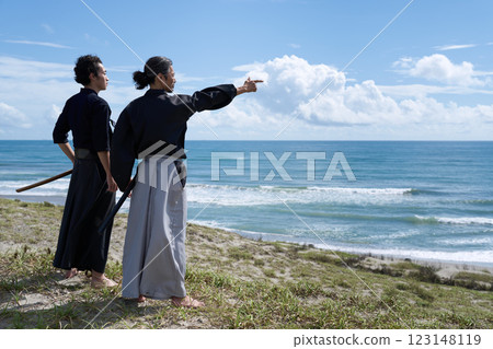 Back view of two men holding swords and looking out to sea Back view of two men holding swords and looking out to sea 123148119