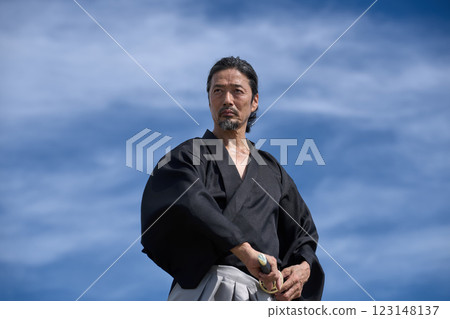 A man in kimono holding a sword under a blue sky 123148137