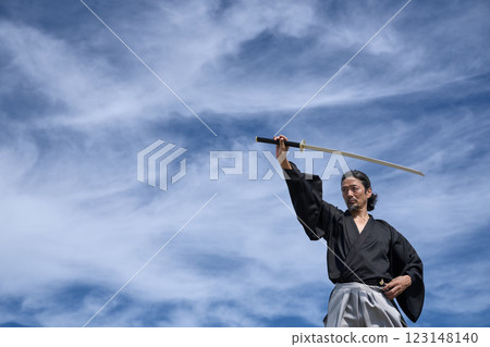 A man in kimono holding a sword under a blue sky A man in kimono holding a sword under a blue sky 123148140
