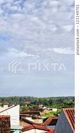 Tranquil view of a serene village with red-tiled roofs, surrounded by greenery, under a partly cloudy sky. Captures peaceful rural living and a connection to nature. 123149701