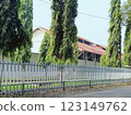 Greenery enhances this tranquil area with tall trees by a fence near a house, providing a peaceful suburban aesthetic surrounded by nature. 123149762