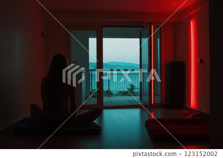 Woman meditating in evening near open balcony with cityscape and red lights 123152002
