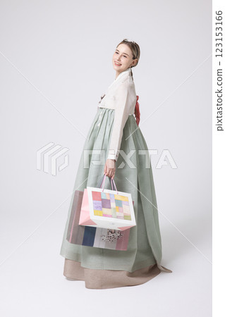 A Western woman standing wearing a Hanbok and holding shopping bags 123153166