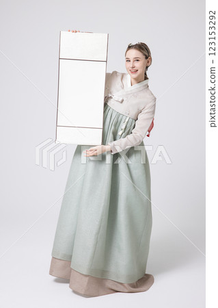 A Western woman standing wearing a Hanbok and holding a hanging scroll 123153292